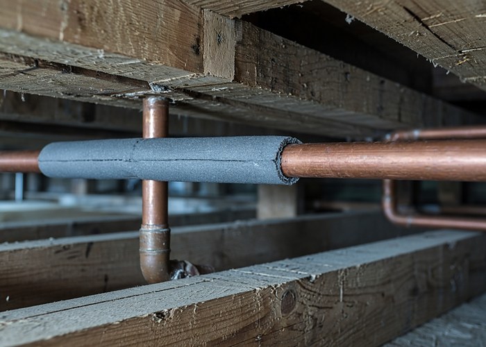 Copper water pipes under floor joists with foam insulation fitted over part of the run and bare copper continuing past it