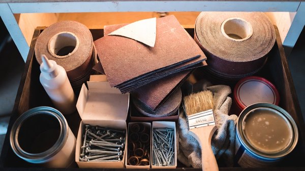 An open drawer of sandpaper, glue, screws and tins of finish
