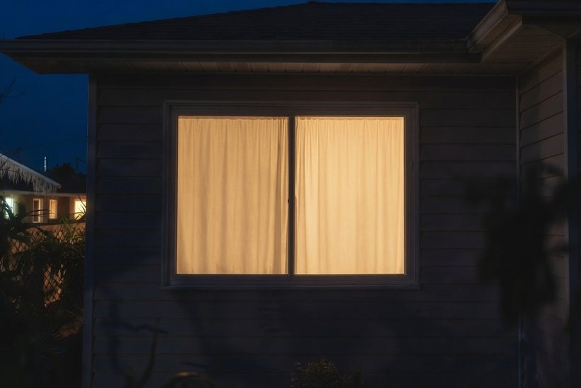 The same window at night with the curtains drawn, showing only a warm even glow
