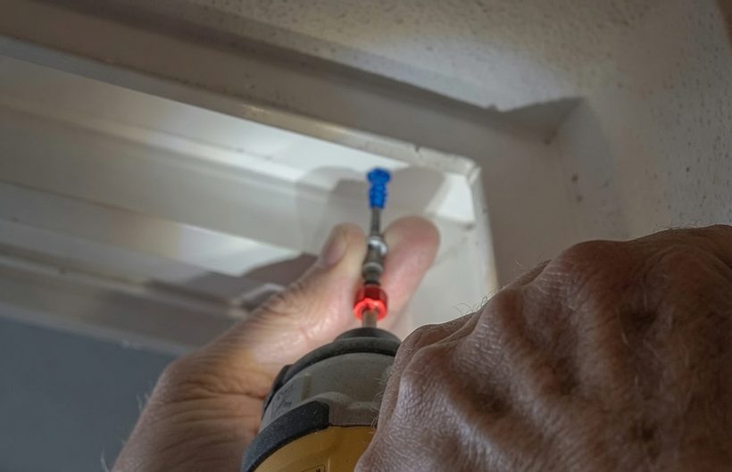 A hand using a cordless driver to set a screw partway into the upper track of a sliding door frame